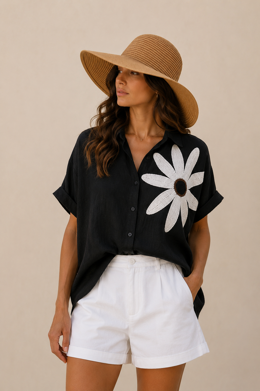 Woman wearing a black shirt with a white daisy design, white shorts, and a straw hat.